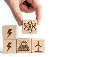Hand placing wooden cube with atomic energy symbol among renewable energy icons including solar panel and wind turbine on white background.