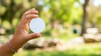 Hand holding blank white circle against blurred green park background, suitable for logo mockups, branding presentations, and product display concepts.