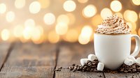 Hot chocolate topped with whipped cream and cocoa powder in white mug on rustic wooden table with coffee beans and marshmallows against blurred golden bokeh lights.