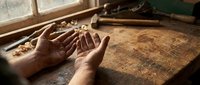 Craftsman hands shaping wood with chisels and tools on workbench, demonstrating traditional woodworking techniques and artisan skills in workshop setting.