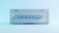 Approved stamp with blue letter tiles in transparent acrylic box on light background, suitable for business approval concepts and office design projects.