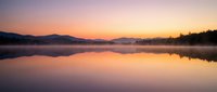 Serene lake at sunrise with misty mountains reflected in calm water, golden and pink sky, peaceful nature landscape for meditation and relaxation.