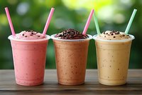 Three colorful fruit smoothies with chocolate chips and straws on wooden table against blurred green background for healthy beverage menu design.