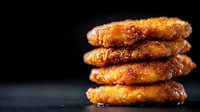 Homemade caramelized sugar cookies stacked in pile on dark background with copy space. Golden brown treats with crispy glazed coating and soft center.