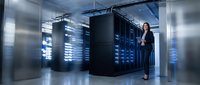 Young woman in business attire standing in modern data center with illuminated server racks, suitable for technology, IT infrastructure, and corporate computing concepts.