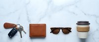 Everyday carry essentials arranged on marble surface including leather wallet, car keys, sunglasses and coffee cup for modern lifestyle flatlay.