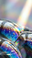 Iridescent soap bubbles with rainbow reflections and water droplets creating prismatic light effects and colorful spectrum patterns on translucent surface.