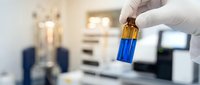 Laboratory technician in white gloves holding blue liquid sample vial in modern medical research facility for scientific analysis and testing.