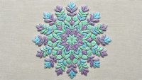 Intricate mandala snowflake embroidery in purple and teal threads on beige fabric background for winter holiday crafts and textile design projects.