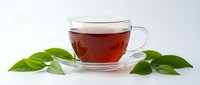 Glass cup of hot black tea with fresh green leaves on white background, perfect for healthy lifestyle and beverage concepts.