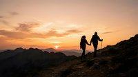 Two hikers with trekking poles ascending a mountain ridge at sunset, silhouetted against golden sky and distant peaks, capturing adventure and outdoor exploration.