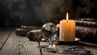Mystical fortune telling setup with burning candle, crystal ball, tarot cards and ancient books on wooden table for divination and spiritual guidance.