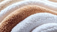 Soft white and beige cotton towels rolled in waves creating abstract texture pattern. Clean fresh spa bathroom linens with detailed terry cloth surface.