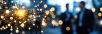 Glowing sparkler with bright golden sparks against blurred silhouettes and bokeh lights creating festive holiday atmosphere at dusk celebration.