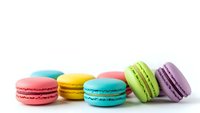 Colorful French macarons in row on white background. Sweet pastry desserts with vibrant shells in pink, yellow, blue, green and purple colors isolated.