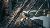 Modern glass office building facade with geometric steel framework reflecting urban cityscape during golden hour lighting for corporate architecture design.