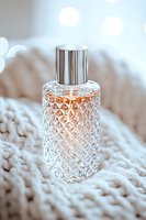Crystal glass perfume bottle with silver cap on soft knitted texture background. Delicate peach-colored liquid inside creates elegant luxury atmosphere with bokeh lights.