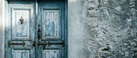 Weathered blue wooden doors with peeling paint on rustic stone wall. Vintage Mediterranean architecture detail for renovation and restoration projects.