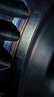 Close-up macro shot of industrial metal gear teeth with iridescent rainbow oil film coating creating colorful reflections on dark steel surface.
