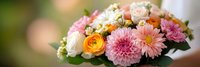 Elegant mixed flower bouquet with pink dahlias, orange ranunculus, white roses and greenery arranged for wedding, celebration or romantic gift occasions.