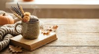 Cozy autumn still life with ceramic mug, dried flowers, knitted sweater and open book on rustic wooden table. Warm seasonal home decor for relaxation.