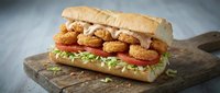 Crispy fried chicken sandwich with fresh lettuce and tomato on crusty bread roll served on rustic wooden cutting board for restaurant menu design.