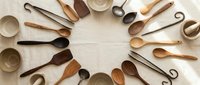 Wooden kitchen utensils and bowls arranged in circular pattern on white background. Natural wood cooking tools for culinary preparation and serving.