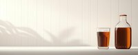 Glass and bottle filled with dark liquid on white surface with soft shadow pattern, minimalist composition for beverage advertising and product photography.