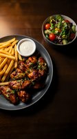 Grilled chicken wings with french fries and dipping sauce served alongside fresh mixed greens salad on wooden table for restaurant menu photography.