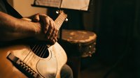 Musician with brown skin playing acoustic guitar in warm studio lighting, suitable for music education, performance promotion, and creative industry content.