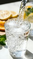 Fresh sparkling water pouring into a glass with bubbles, lemon slices and mint in the background, healthy hydration concept.