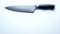 Sharp chef knife with Damascus steel blade and black handle on white background for culinary and kitchen design projects.