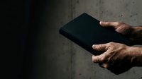 Male hands holding black tablet device against concrete wall background for technology and business concepts.