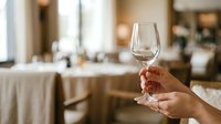 Woman holding empty wine glass in upscale restaurant dining room with elegant table settings and soft lighting for hospitality and fine dining concepts.