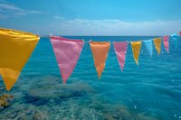 Colorful triangle bunting flags against turquoise ocean water and blue sky background. Perfect for summer party decoration, beach celebration, or festive coastal events.
