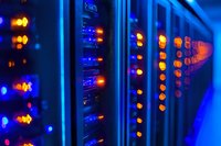 Server room with glowing blue and orange LED indicators on network equipment, data center interior showing modern technology infrastructure in dark ambient lighting.