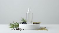 Clear glass bottle with pump dispenser surrounded by pine branches and peppercorns on white platform against neutral background for skincare branding.