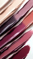 Diagonal smears of liquid lipstick in various shades from nude pink to deep burgundy on white background, showing texture and consistency of cosmetic products.