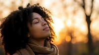 Young African American woman with curly hair enjoying peaceful moment outdoors during golden hour sunset with eyes closed and serene expression.
