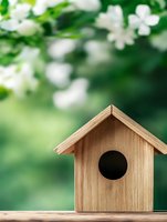 Wooden birdhouse on garden table against blurred spring background with white flowering branches, soft bokeh effect and natural green backdrop.
