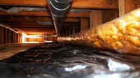 Crawl space under house showing insulation, vapor barrier, and ductwork in residential foundation. Low angle view captures construction details and home maintenance.