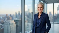 Confident senior businesswoman in navy suit standing by office windows with city skyline view, representing corporate leadership and professional success.