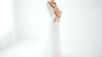 Pregnant woman in white dress holding baby shoes against white background, maternity concept for family planning and motherhood announcements.