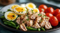 Fresh tuna salad with boiled eggs, green beans, and cherry tomatoes on dark plate, perfect for healthy protein-rich meal.