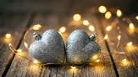 Silver glittery heart-shaped ornaments surrounded by warm golden fairy lights on rustic wooden surface for holiday decorating and festive celebrations.