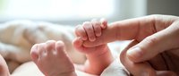 Newborn baby tiny hand grasping adult finger, close-up shot capturing tender bond between parent and child in soft natural light.