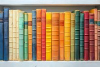 Colorful vintage hardcover books arranged in row on white bookshelf, displaying rainbow spectrum of spines from blue to red and yellow.