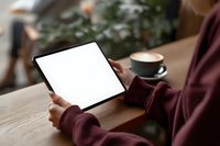 Woman holding blank tablet screen with coffee cup on wooden table in cozy cafe setting for digital mockup presentations and app development showcases.