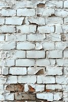 Old white painted brick wall with peeling paint and damaged surface showing weathered texture and exposed red bricks underneath.
