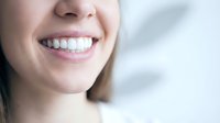 Close-up of young woman's radiant smile showing perfect white teeth in bright dental office setting for oral health and cosmetic dentistry concepts.